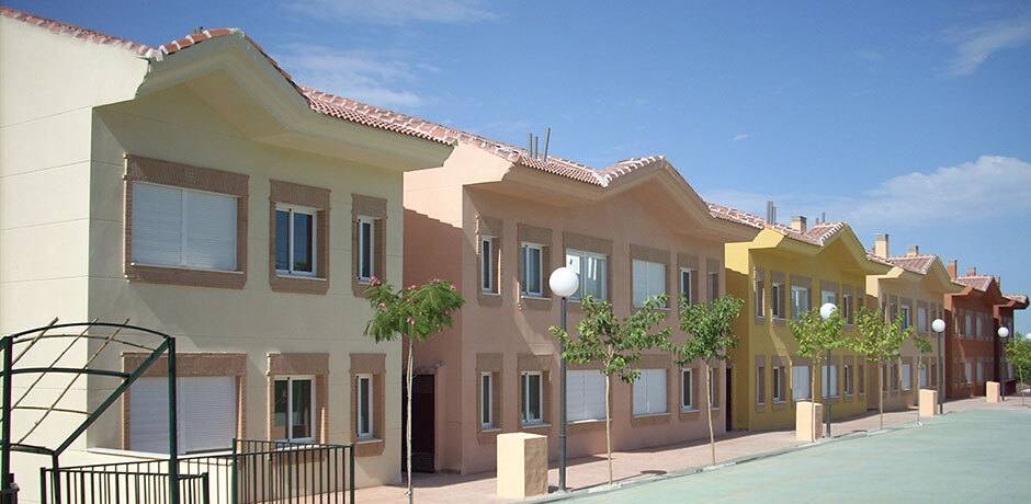 Fachada del conjunto residencial de dos plantas con módulos en tonos ocre y salmón a lo largo de una calle con árboles jóvenes.