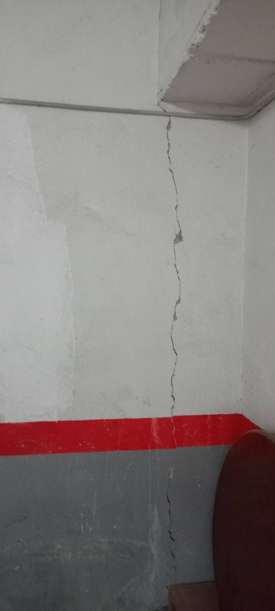 Grieta vertical que atraviesa de arriba abajo un muro pintado del garaje, cruzando la franja roja del zócalo.