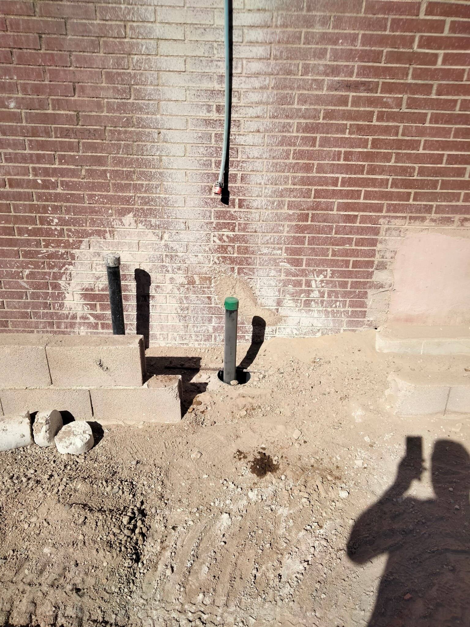 Bocas de tubos de inyección asomando del terreno al pie de un muro de ladrillo.