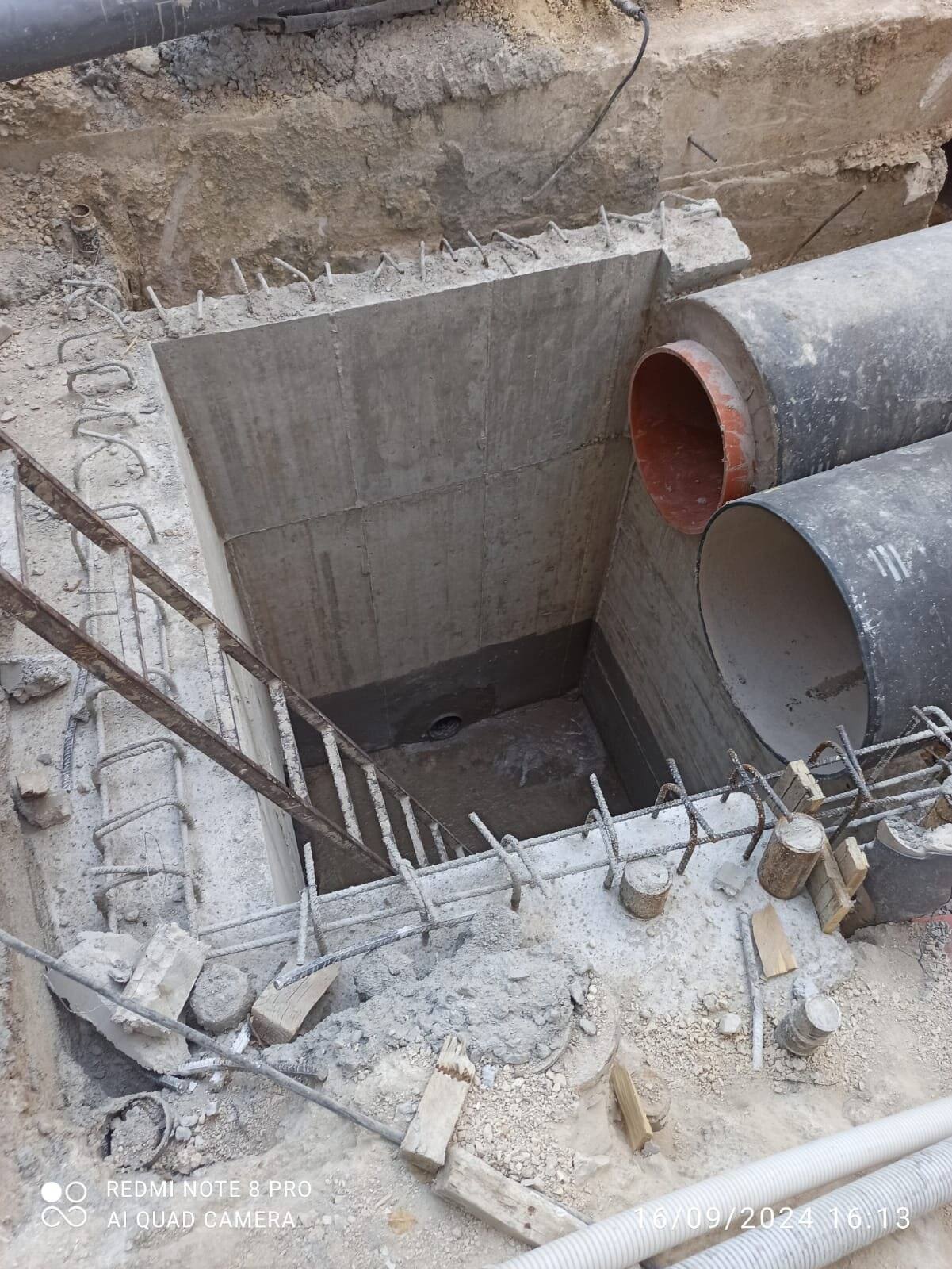 Concrete chamber under construction with timber formwork and reinforcement, with two pipes passing through it.