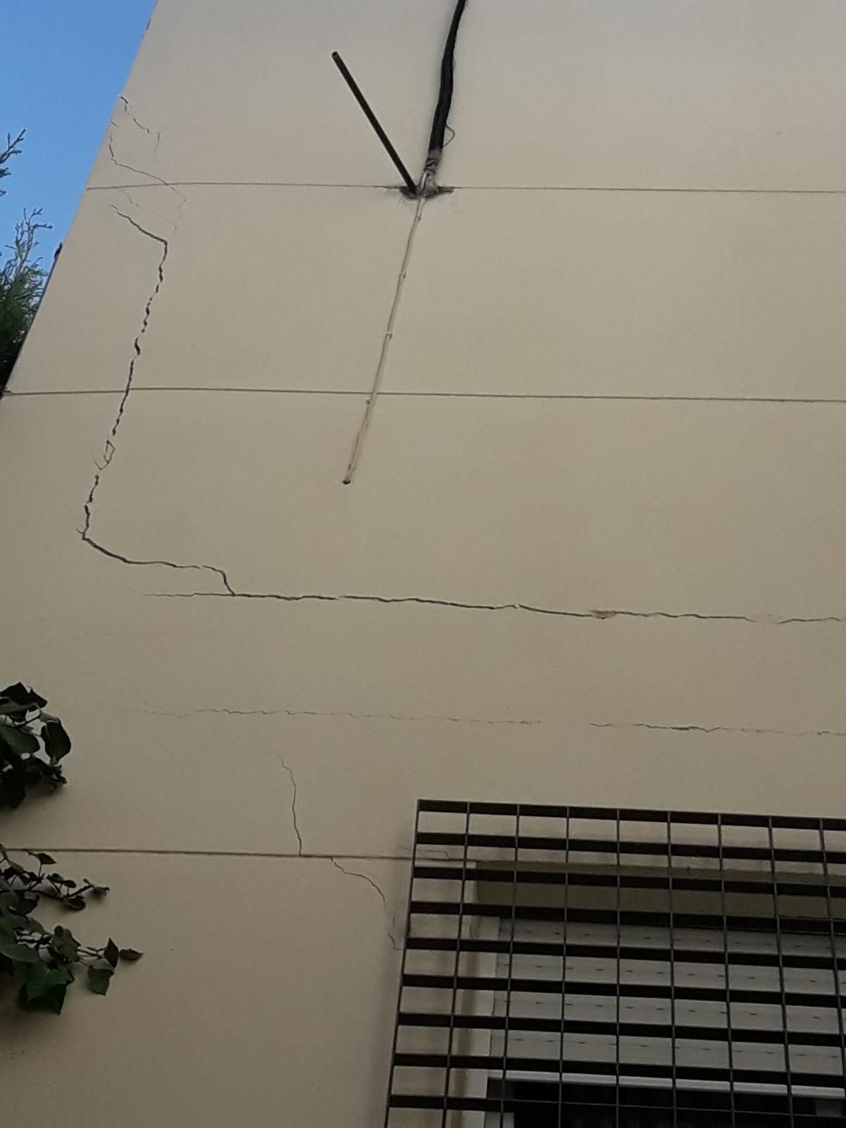 Fachada enfoscada recorrida por una grieta escalonada que baja hacia el dintel de una ventana con reja.