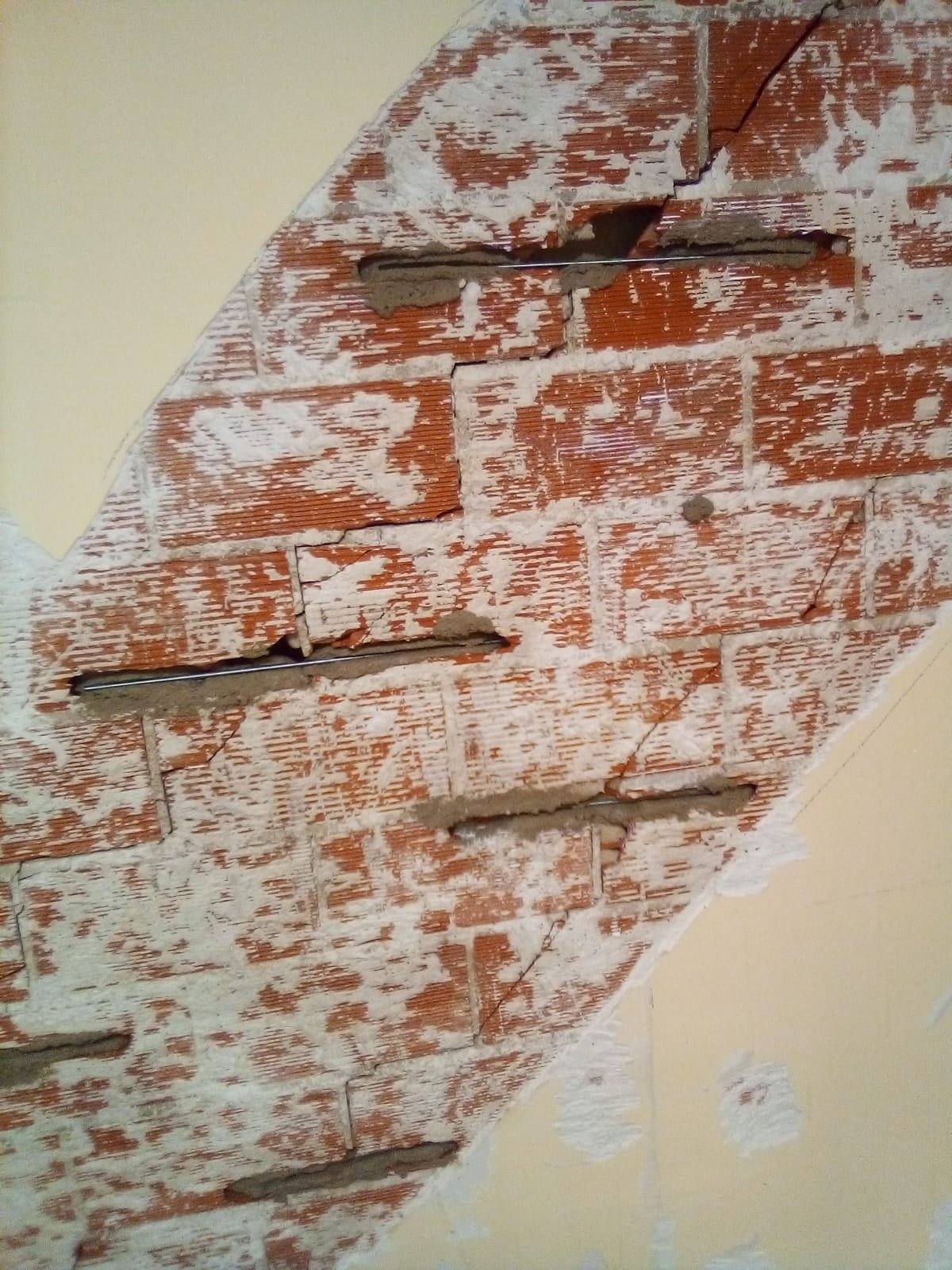 Muro de ladrillo con el enlucido picado a lo largo de una grieta diagonal, cosida con grapas metálicas perpendiculares.