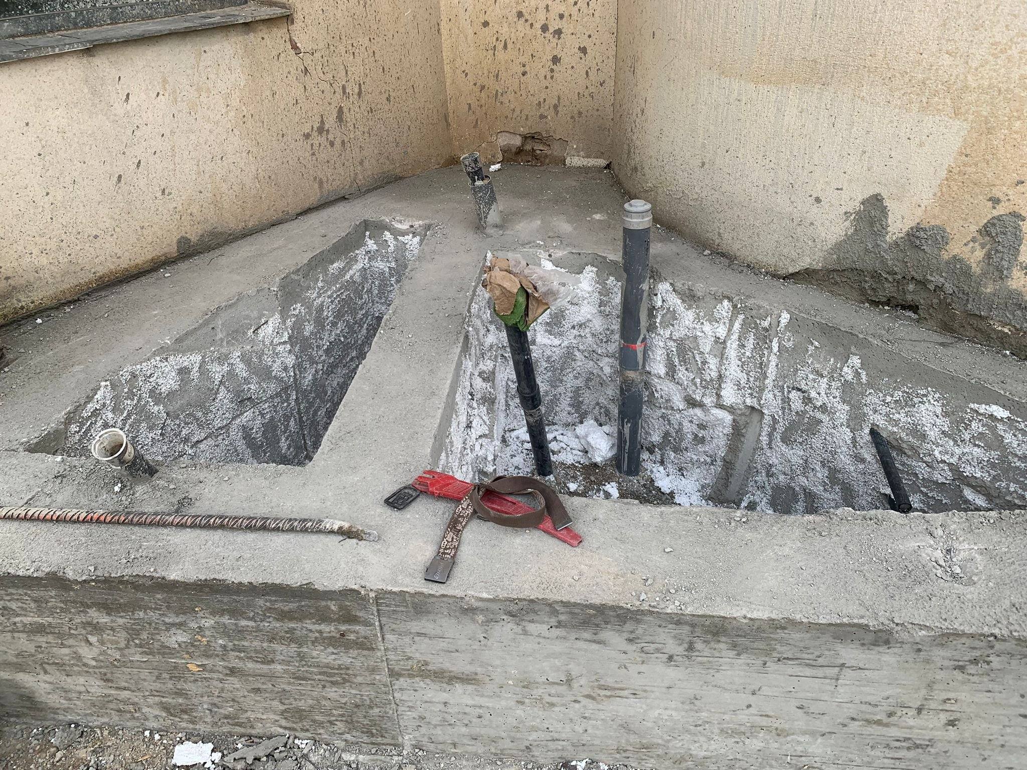 Zanjas abiertas al pie de un muro curvo, con tubos de inyección verticales asomando del terreno tratado.