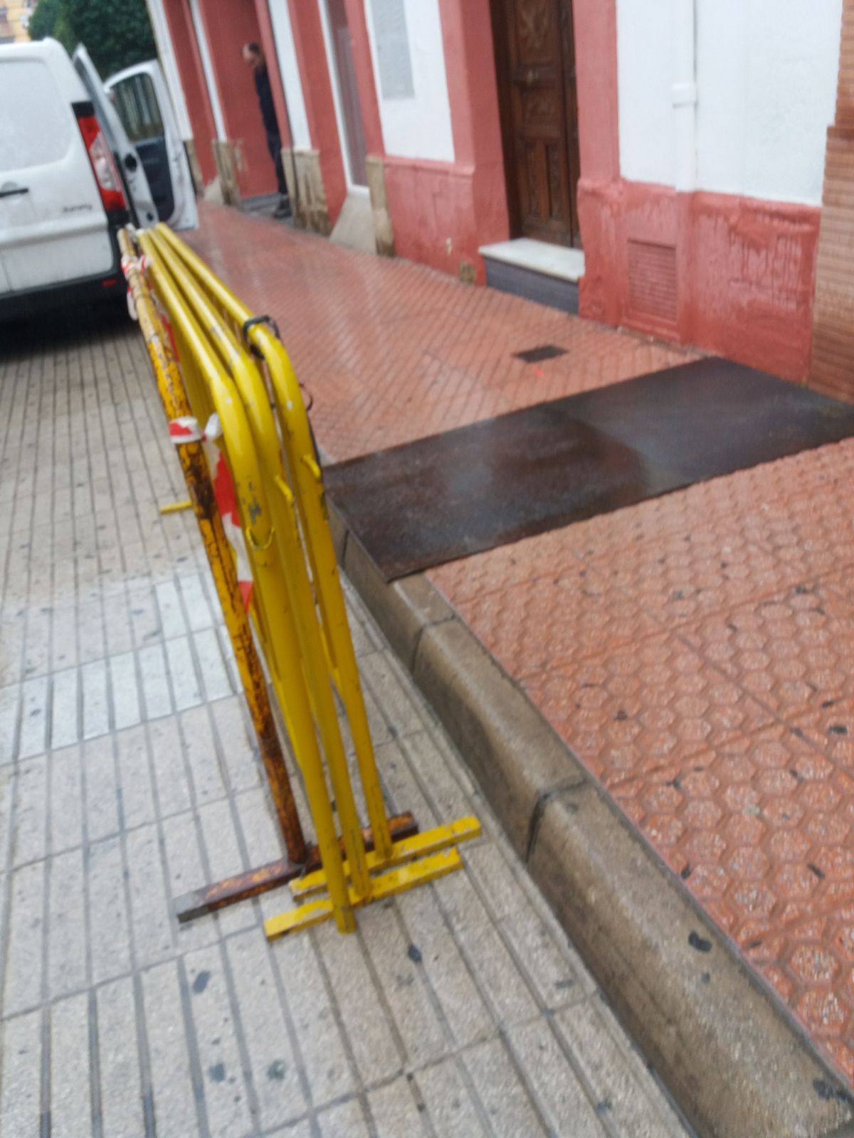 Acera con vallas amarillas de obra y la reposición de pavimento sobre la zanja recién cerrada de una canalización.